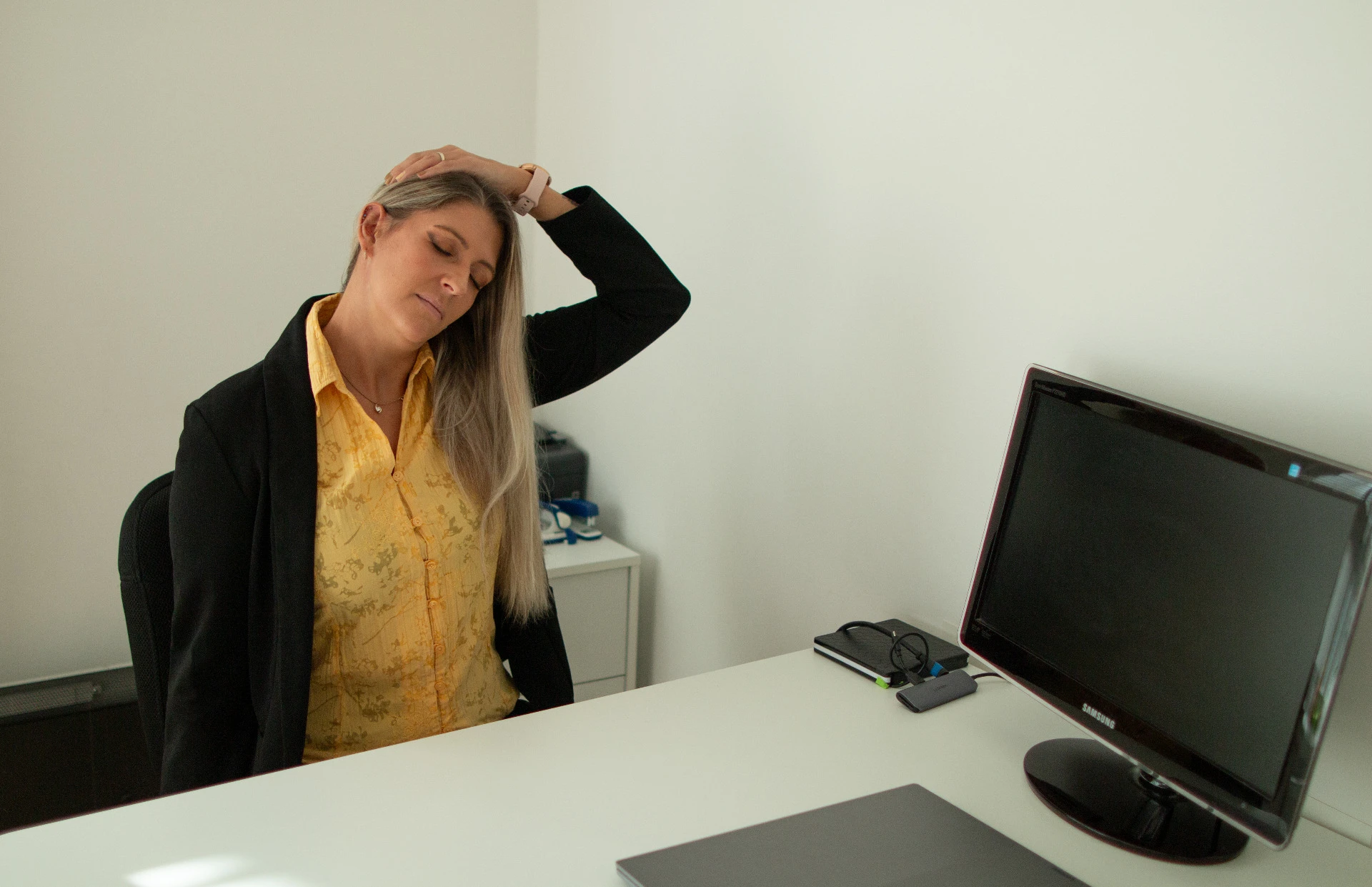 Eine Frau dehnt am Büroschreibtisch mit geschlossenen Augen ihren Nacken