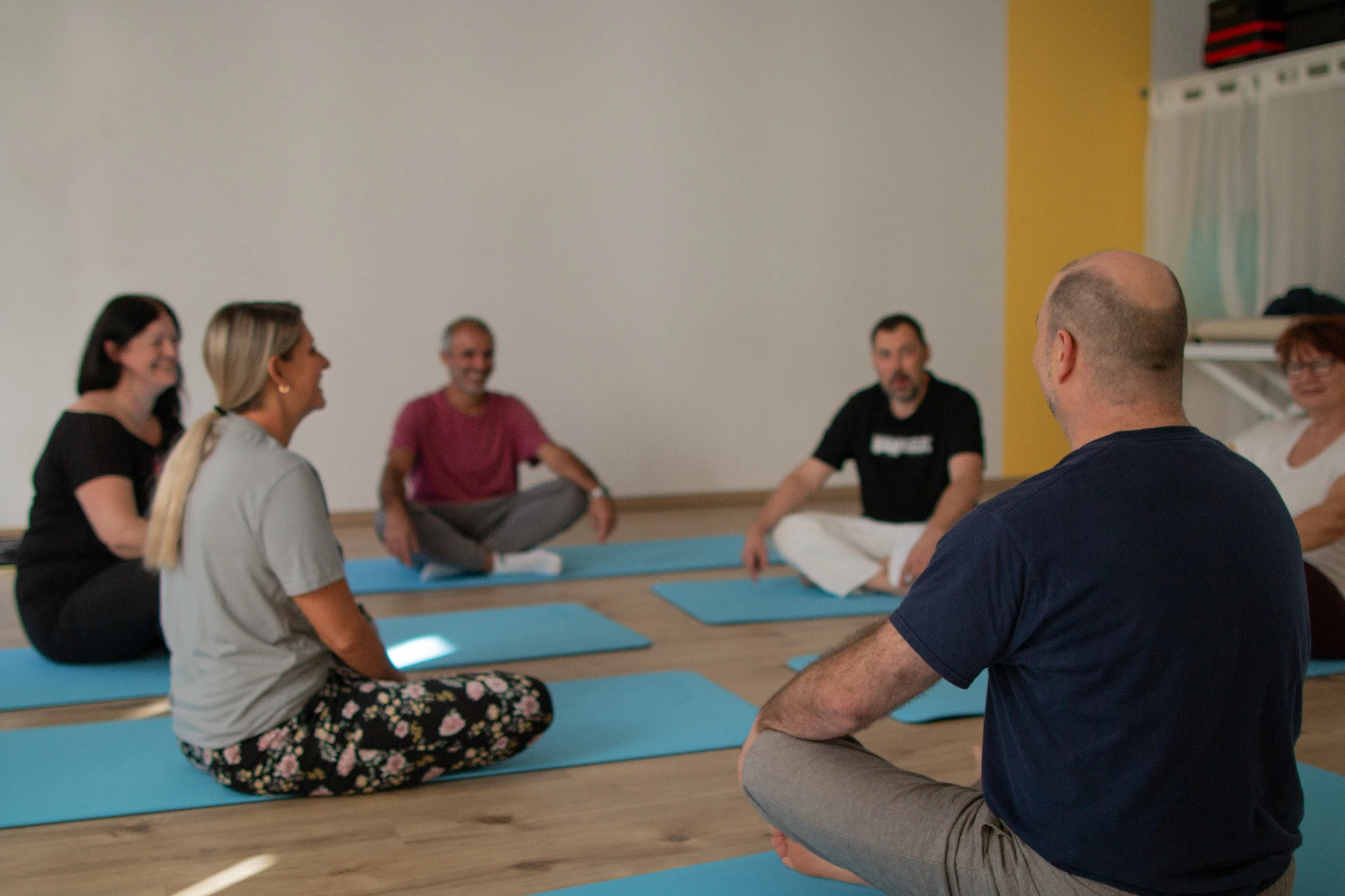 Die Qigong-Gruppe sitzt lachend im Kreis auf den Matten, Gregor Chaloupka im Vordergrund von hinten