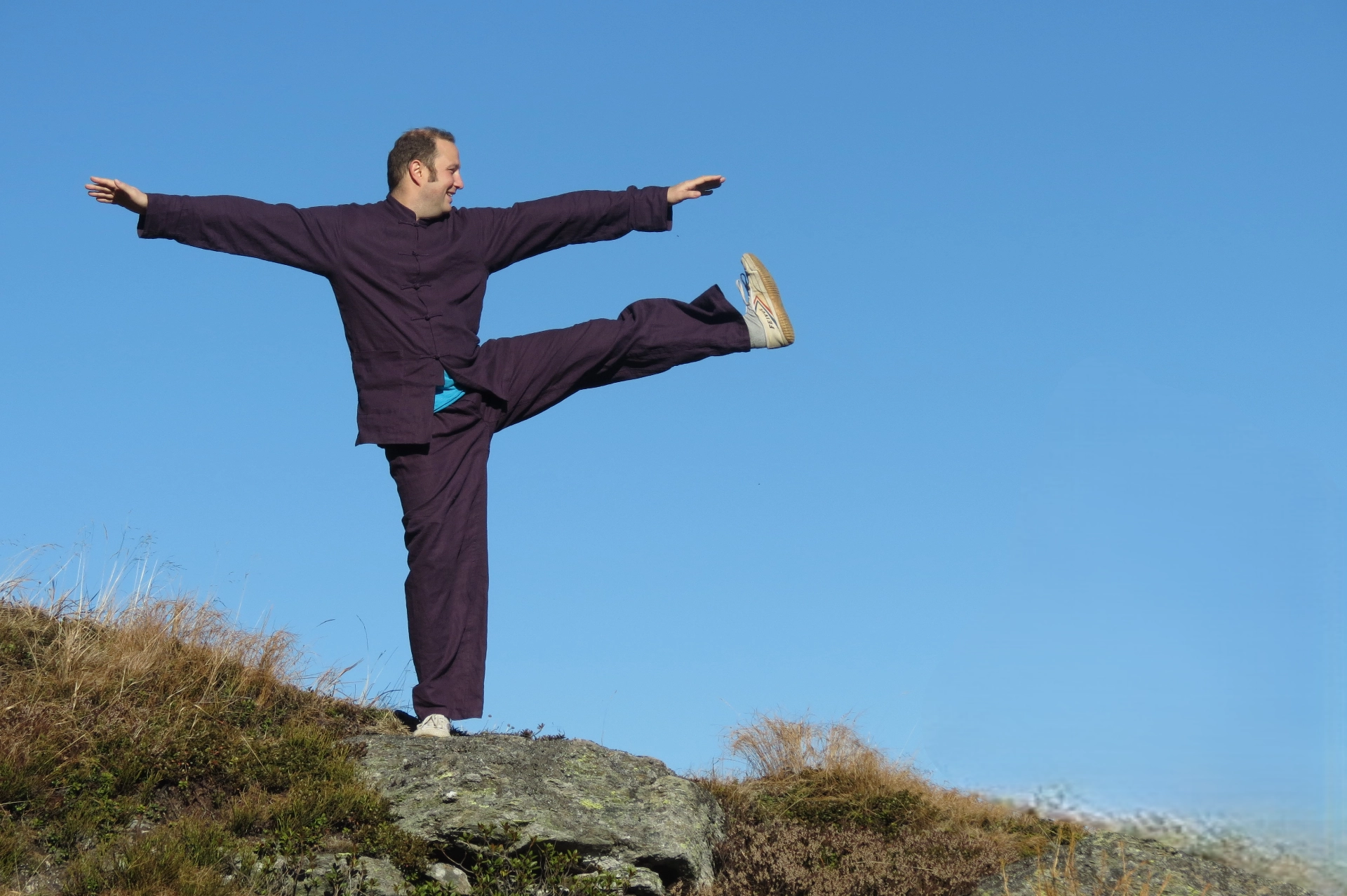 Gregor Chaloupka bei einer Taiji-Bewegung mit Tritt vor blauem Himmel