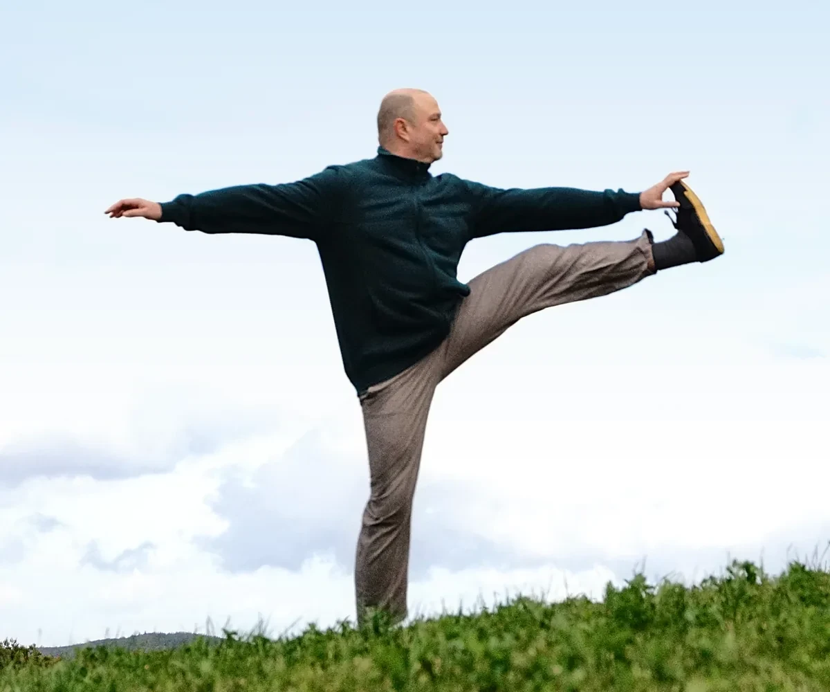 Gregor Chaloupka in einer Balance-Haltung mit seitlich gestrecktem Bein auf einer Wiese unter hellem Himmel